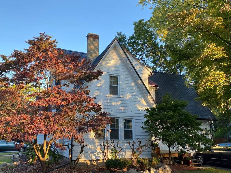 Before: the house with white siding, a black metal roof and a red Japanese maple out front, before exterior painting